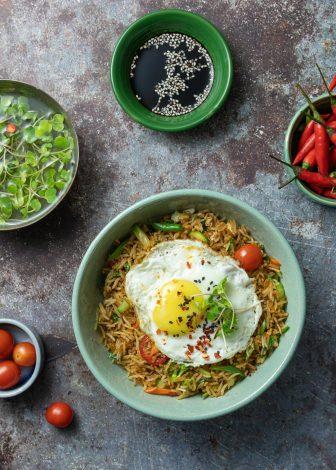 Top view of Asian fried rice with egg, vegetables, and sauces on rustic background.